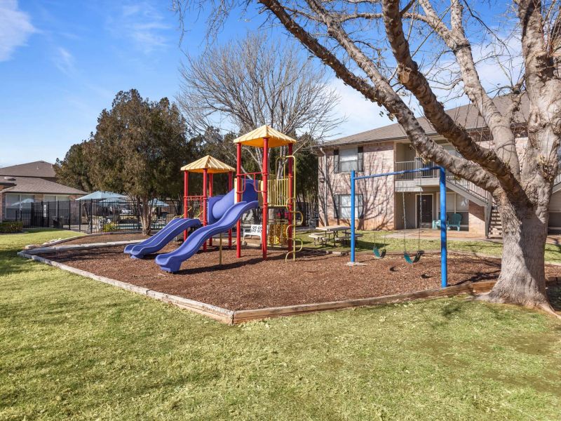 Encino Park Apartments community playground with large colorful play structure surrounded by green grass area