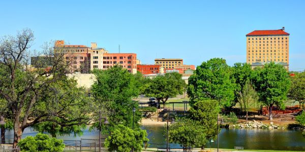 San Angelo, TX skyline with trees and a pond in the foreground under a clear blue sky.