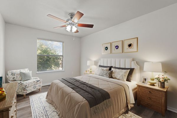 Cozy bedroom at Encino Park with a double bed, patterned armchair, wooden nightstands, and a ceiling fan.